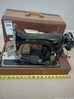 Full view of sewing machine on wooden base with tape measure for scale, case behind