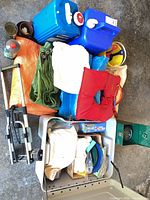 Overall lot view showing life jacket, tarps, hand truck, water jugs, storage tote with contents