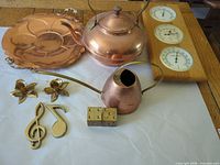 All items grouped: copper kettle, watering can, tray; brass candle holders, music note hooks, dice; wooden weather station