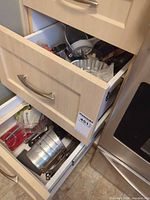 Open drawers displaying assorted kitchen utensils and bakeware as listed