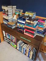 Front view of cabinet with multiple stacks of books on top and shelves filled