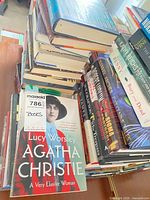 Stacks of hardcover and paperback books with visible titles and maxsold lot tag