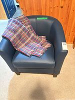 Front view of navy faux leather club armchair with plaid throw