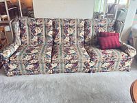 Front view of floral tapestry sofa with two red throw pillows