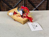 Front view of Sorcerer Mickey ornament on open book with tag visible