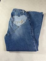 Folded jeans showing heart patch and embroidered logo