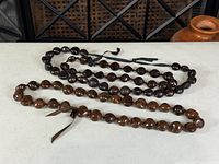 Three kukui nut leis laid flat showing color variation and ribbon ties