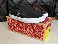 Side view of black perforated leather Vans Slip-On shoes on original box