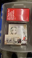 Red retail box labelled 12-Piece Set Porcelain Christmas Dinnerware inside storage tote