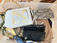 Overview of assorted bags in storage bin including white geometric bag, sequined clutch, patent clutches and others