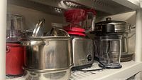Group view of cookware, appliance pitchers, rice cooker base and plates on shelf