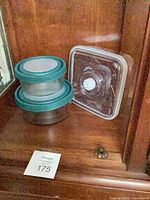 Stacked round glass containers with teal lids beside square vacuum lid