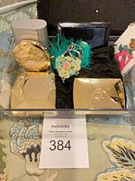 Tray showing both gold-tone compacts, enamel keychain with teal tassel, printed tag keychain