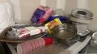 Lot overview showing cake pans, steamer inserts, cake carrier, muffin pan, baking racks, red cups and misc items