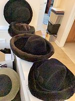 Three black hats arranged on ledge; front fedora, two fur-trim hats behind