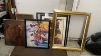 Group of art pieces leaning against wall showing canvas portrait, black-framed musicians print, two smaller framed child prints, empty gold frame