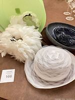White tulle hat, feathered headpiece, grey felt beret inside view, pale green hat form visible