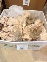 Box containing assorted holly pattern and clear glass tumblers wrapped in paper