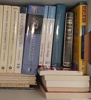 Books upright: spines showing Mastering the Old Testament volumes, God’s Loving Word, two Revelation commentaries, Charles Hodge volumes, Holy Bible; horizontal stack beneath