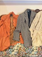 Three jackets laid out: orange blazer, houndstooth coat, beige jacket