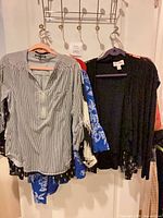 Group of tops on hangers: striped blouse, black cardigan, blue floral garment visible