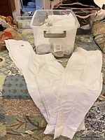 White pants spread out with additional folded pants and plastic tote