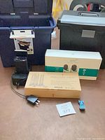 Lot overview showing storage totes, Arlo camera box, candle set box, power accessories and toy