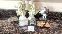 Group shot of all items: pair cherub candlesticks, metal dish, packaged music box, glass keepsake, copper plaque, knight on unicorn figurine