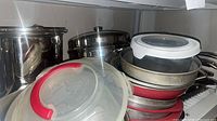 Stacked cookware showing red pans, stainless pans, plastic storage lids