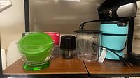 Shelf view with Ninja motor base, green-lidded bowl, several small cups