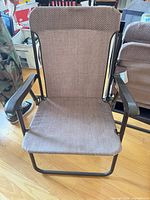 Front view of single brown folding chair showing fabric seat, backrest and armrests