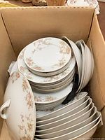 Stack of dinner and salad plates, bowls, and covered tureen lid showing pink floral and gold trim pattern