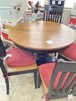 Round oak top pedestal table with four black chairs and red cushions
