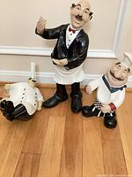Group view of three resin chef figurines in various poses on wood floor