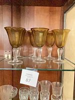 Six amber bowl goblets with clear stems on shelf