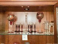 Shelf view showing both oversized poinsettia goblets, eight cordial glasses, tall clear flute and four clear wine glasses