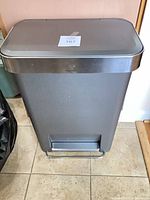 Front view of charcoal gray slim step trash can showing stainless steel foot pedal and lid trim