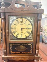 Front view of wood mantel clock showing dial, glass door, turned columns and scrolled top