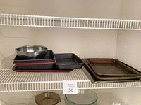 Stacked stainless steel mixing bowl atop three black nonstick pans with red silicone liners, adjacent metal baking sheets