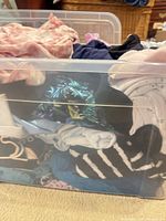 Plastic tote with mixed women’s garments visible including palm-leaf print, white ribbed, black and striped pieces