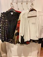 Group of cardigans and jackets on hangers: black openwork, abstract print, white knit