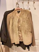 Tan laser-cut jacket hanging in front of black garment