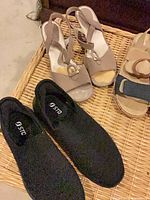 Black STQ sneakers and two sandal pairs on wicker surface