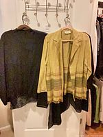 Two garments on hangers: yellow striped-hem cardigan and black long-sleeve top