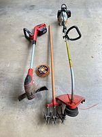 Overview of Stihl gas trimmer, Black+Decker cordless trimmer with battery, wooden cultivator, and trimmer line spool on concrete floor