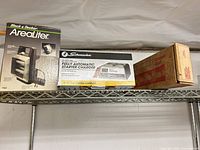 Three boxed items on shelf: Black & Decker AreaLiter light, Schumacher battery charger, grease gun