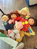 Box containing five Cabbage Patch Kids dolls with various outfits and loose clothing
