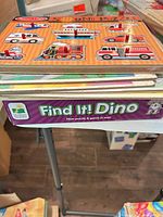 Stack of puzzles showing top wooden vehicles sound puzzle and box side of Find It! Dino floor puzzle