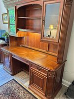 Front view of Hooker wood desk with lighted hutch showing upper glass cabinets, center shelving, lower desk with keyboard drawer and side cabinets