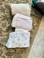 Folded cream fleece throw, pink flannel sheets, snowman flannel sheets displayed on rug and tile floor